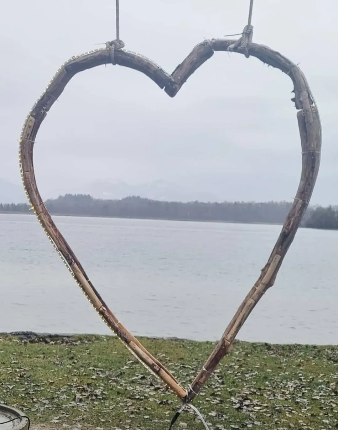 Ein großes Herz aus Holz und Ästen hängt an einem Seeufer als Symbol für Liebe und Erinnerung. Herzenssprecherin Caroline Stiegler, Trauerbegleitung und freie Rednerin in Salzburg.